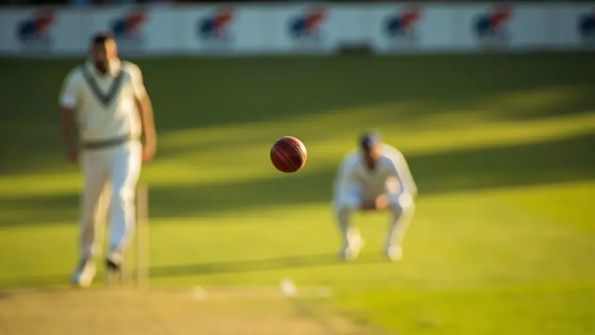 Editorial cricket photography of a Test match in progress on an Indian ground, a red ball mid-flight above the pitch